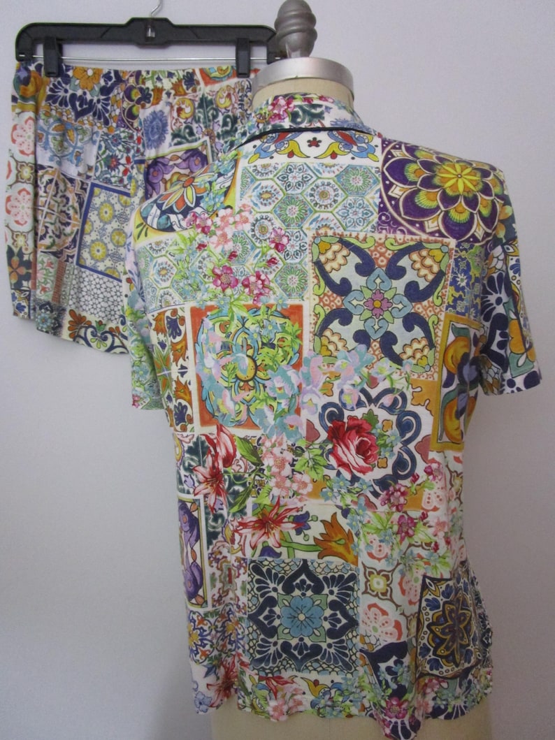 Puede incluir: Un conjunto de camisa de manga corta con botones y pantalones cortos a juego con un estampado de patchwork vibrante y multicolor. El patr&oacute;n consiste en varios dise&ntilde;os de azulejos geom&eacute;tricos, motivos florales y volutas intrincadas en tonos azul, amarillo, rojo, verde y morado sobre un fondo blanco.