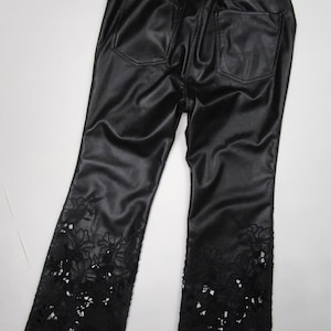 Pu&ograve; includere: Pantaloni in similpelle nera con elastico in vita e due tasche posteriori. La parte inferiore di ogni gamba &egrave; decorata con intricati intagli in pizzo floreale nero che si estendono da met&agrave; polpaccio fino all'orlo del capo di abbigliamento.