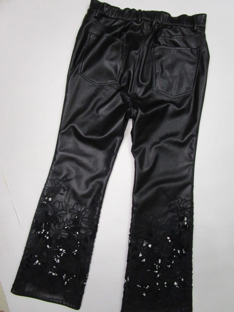 Pu&ograve; includere: Pantaloni in similpelle nera con elastico in vita e due tasche posteriori. La parte inferiore di ogni gamba &egrave; decorata con intricati intagli in pizzo floreale nero che si estendono da met&agrave; polpaccio fino all'orlo del capo di abbigliamento.
