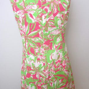 May include: Sleeveless dress with a vibrant floral pattern in pink, green, and white. The dress is displayed on a mannequin, showcasing its form-fitting design. The fabric features a repeating botanical print.
