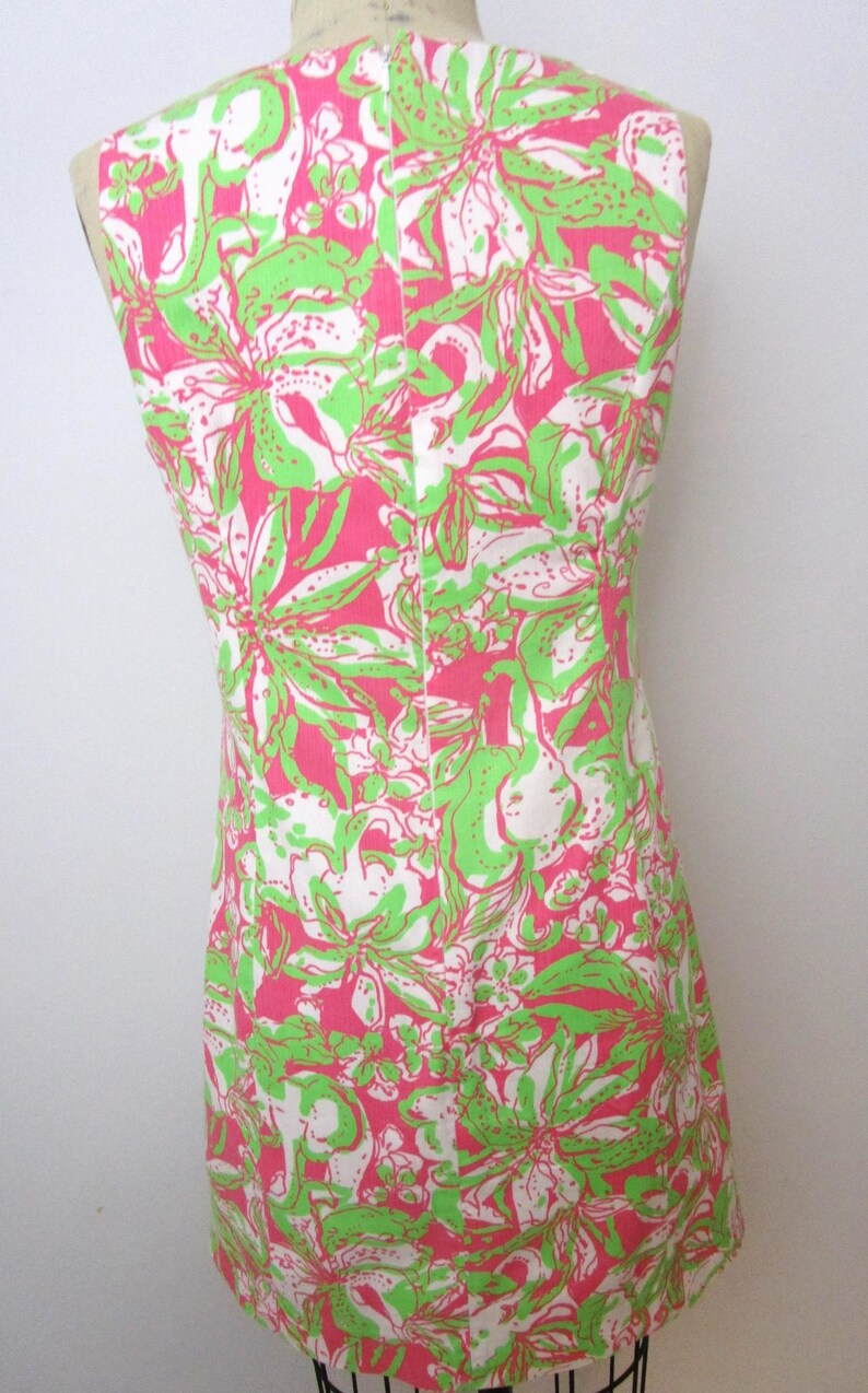 May include: Sleeveless dress with a vibrant floral pattern in pink, green, and white. The dress is displayed on a mannequin, showcasing its form-fitting design. The fabric features a repeating botanical print.