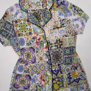 Puede incluir: Una camisa de pijama de manga corta con botones y un vibrante patr&oacute;n de azulejos multicolor en tonos azul, amarillo, morado y verde. La camisa tiene un cuello con solapa con ribete negro, un bolsillo en el pecho y botones blancos al frente.