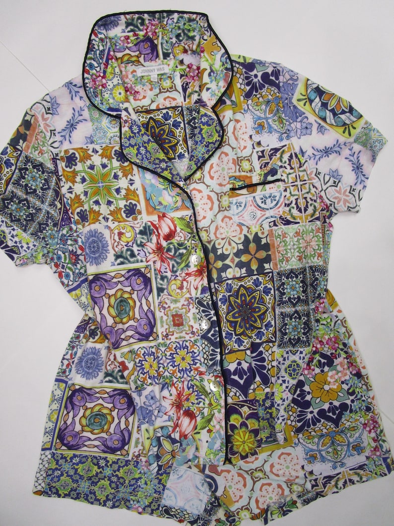 Puede incluir: Una camisa de pijama de manga corta con botones y un vibrante patr&oacute;n de azulejos multicolor en tonos azul, amarillo, morado y verde. La camisa tiene un cuello con solapa con ribete negro, un bolsillo en el pecho y botones blancos al frente.