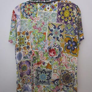 Puede incluir: Una camisa de manga corta con botones que presenta un vibrante patr&oacute;n de patchwork multicolor con diversos dise&ntilde;os florales y geom&eacute;tricos inspirados en azulejos en tonos azul, amarillo, rojo, morado y verde, con un borde oscuro en el cuello.