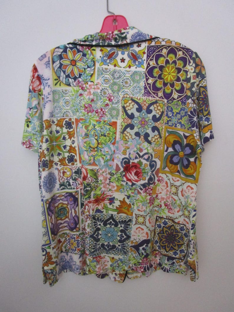 Puede incluir: Una camisa de manga corta con botones que presenta un vibrante patr&oacute;n de patchwork multicolor con diversos dise&ntilde;os florales y geom&eacute;tricos inspirados en azulejos en tonos azul, amarillo, rojo, morado y verde, con un borde oscuro en el cuello.