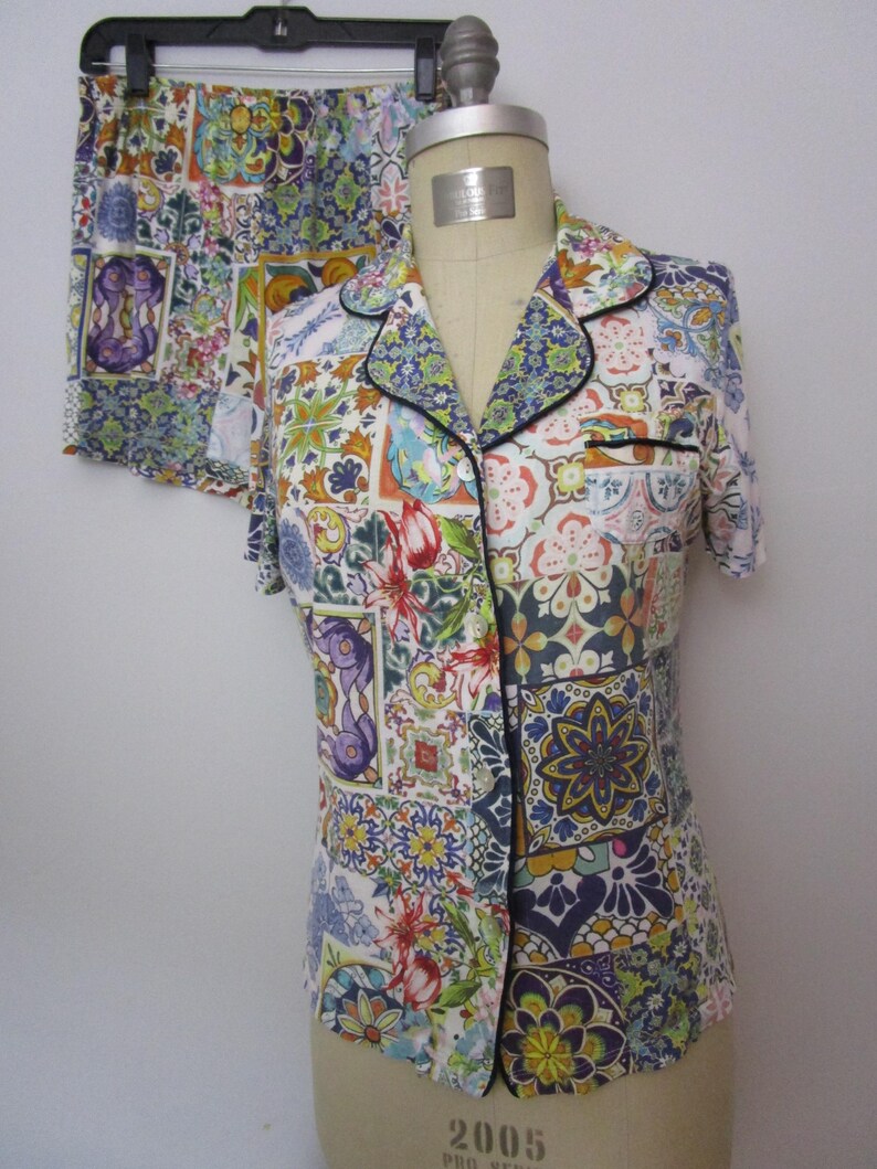 Puede incluir: Un conjunto de camisa de manga corta con botones y pantal&oacute;n corto a juego, con un patr&oacute;n de patchwork multicolor de azulejos florales y geom&eacute;tricos en tonos azul, amarillo, rojo y verde, acabado con ribetes negros en el cuello y bolsillo.