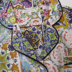 Puede incluir: Una camisa abotonada con cuello de solapa y ribete negro, con un estampado multicolor inspirado en azulejos con motivos florales y geom&eacute;tricos en tonos azul, amarillo, naranja y verde. Una etiqueta blanca muestra el texto JOHNNY WAS.