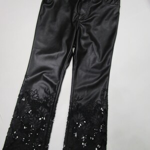 Pu&ograve; includere: Pantaloni neri con finitura liscia e semilucida, dotati di chiusura con bottone e cerniera. La parte inferiore di ogni gamba &egrave; decorata con intricati dettagli in pizzo floreale intagliato che si estendono fino all'orlo del capo.