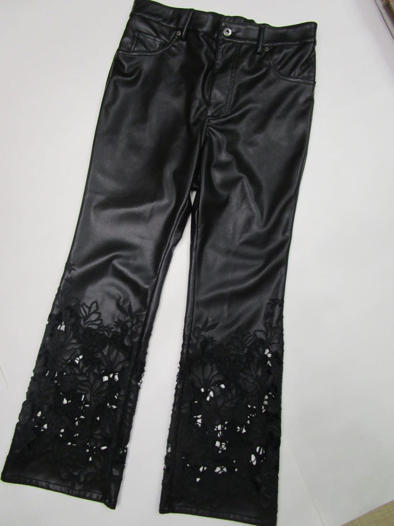 Pu&ograve; includere: Pantaloni neri con finitura liscia e semilucida, dotati di chiusura con bottone e cerniera. La parte inferiore di ogni gamba &egrave; decorata con intricati dettagli in pizzo floreale intagliato che si estendono fino all'orlo del capo.