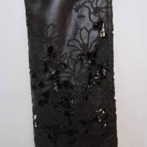 Pu&ograve; includere: Una manica in similpelle nera con intricati motivi floreali tagliati al laser. Il design presenta dettagliati ritagli botanici che creano un effetto pizzo sul materiale scuro, rivelando la superficie sottostante attraverso le aperture.