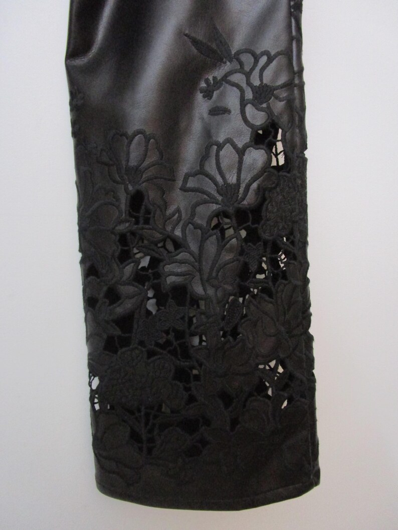 Pu&ograve; includere: Una manica in similpelle nera con intricati motivi floreali tagliati al laser. Il design presenta dettagliati ritagli botanici che creano un effetto pizzo sul materiale scuro, rivelando la superficie sottostante attraverso le aperture.