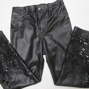 Pu&ograve; includere: Pantaloni neri con una finitura liscia simile alla pelle, dotati di chiusura con bottone e cerniera. La parte inferiore di ogni gamba &egrave; decorata con intricati dettagli in pizzo floreale nero intagliato che si estendono per tutta la larghezza.