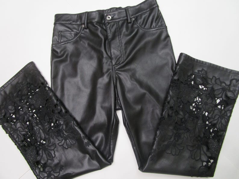Pu&ograve; includere: Pantaloni neri con una finitura liscia simile alla pelle, dotati di chiusura con bottone e cerniera. La parte inferiore di ogni gamba &egrave; decorata con intricati dettagli in pizzo floreale nero intagliato che si estendono per tutta la larghezza.