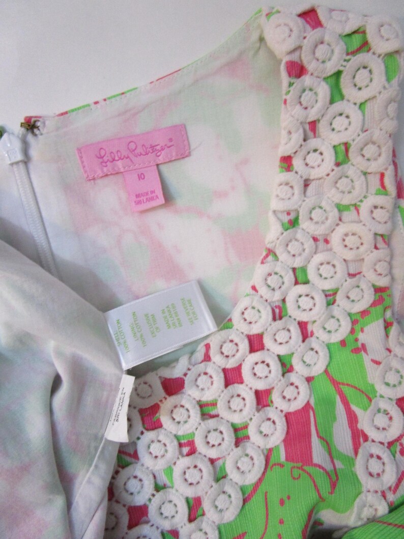 May include: A sleeveless dress with a vibrant floral pattern in pink and green. The dress features a white lace trim around the neckline and a zipper closure. The tag reads "Lilly Pulitzer" and "10".