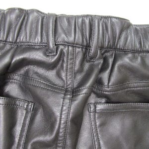 Pu&ograve; includere: Pantaloni in pelle nera con vita elasticizzata e passanti integrati, dettagli con impunture a vista e due tasche posteriori. Il materiale presenta una finitura liscia e leggermente testurizzata con motivi a grana naturale sulla superficie.