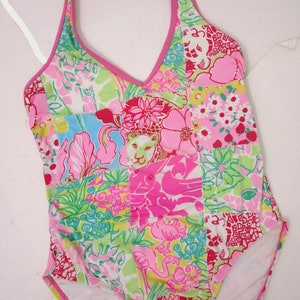 May include: A pink and green halter-style swimsuit with a patchwork design featuring various floral and animal prints. The swimsuit has a V-neckline and a low back.