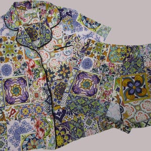 Puede incluir: Un conjunto de pijama de camisa de manga corta con botones y pantal&oacute;n corto a juego, con un vibrante patr&oacute;n de mosaico multicolor de dise&ntilde;os florales y geom&eacute;tricos en tonos morado, amarillo, verde, azul y rosa con ribetes negros.