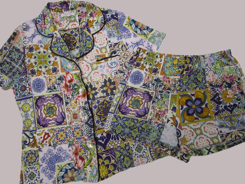 Puede incluir: Un conjunto de pijama de camisa de manga corta con botones y pantal&oacute;n corto a juego, con un vibrante patr&oacute;n de mosaico multicolor de dise&ntilde;os florales y geom&eacute;tricos en tonos morado, amarillo, verde, azul y rosa con ribetes negros.