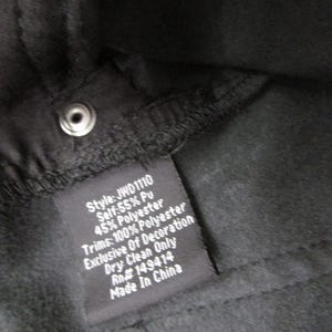 Pu&ograve; includere: L'interno di un capo nero con un'etichetta di manutenzione cucita che riporta il testo bianco: Style: JWD1110, Self: 55% Pu, 45% Polyester, Trims: 100% Polyester, Exclusive Of Decoration, Dry Clean Only, Rn# 149414, Made In China.