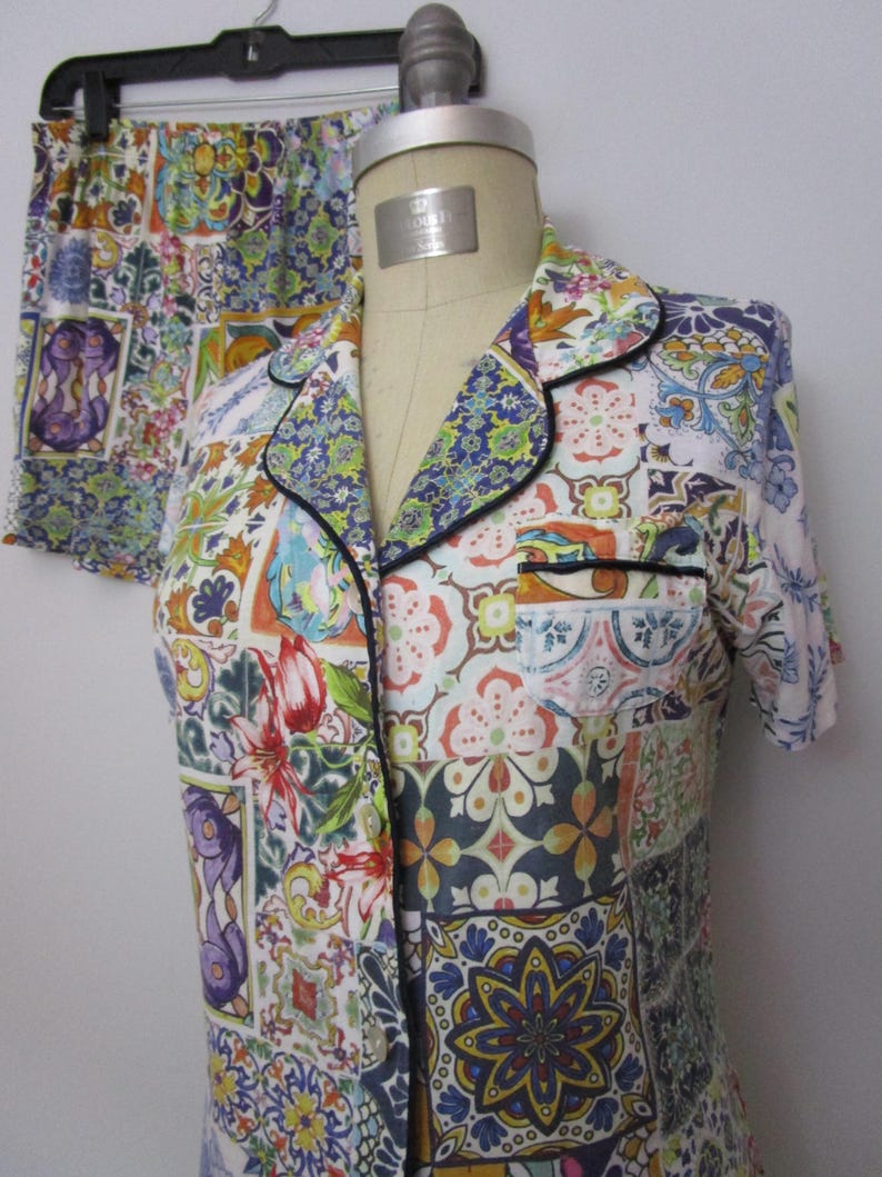 Puede incluir: Un conjunto de pijama de camisa de manga corta con botones y pantal&oacute;n corto a juego, con un estampado multicolor inspirado en azulejos. La camisa incluye un cuello con solapa y ribetes oscuros, un bolsillo en el pecho y cierre frontal.