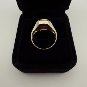 May include: A silver ring with a rectangular, reddish-brown stone set in a classic design. The ring is displayed in a black velvet ring box, showcasing its polished metal and gemstone.