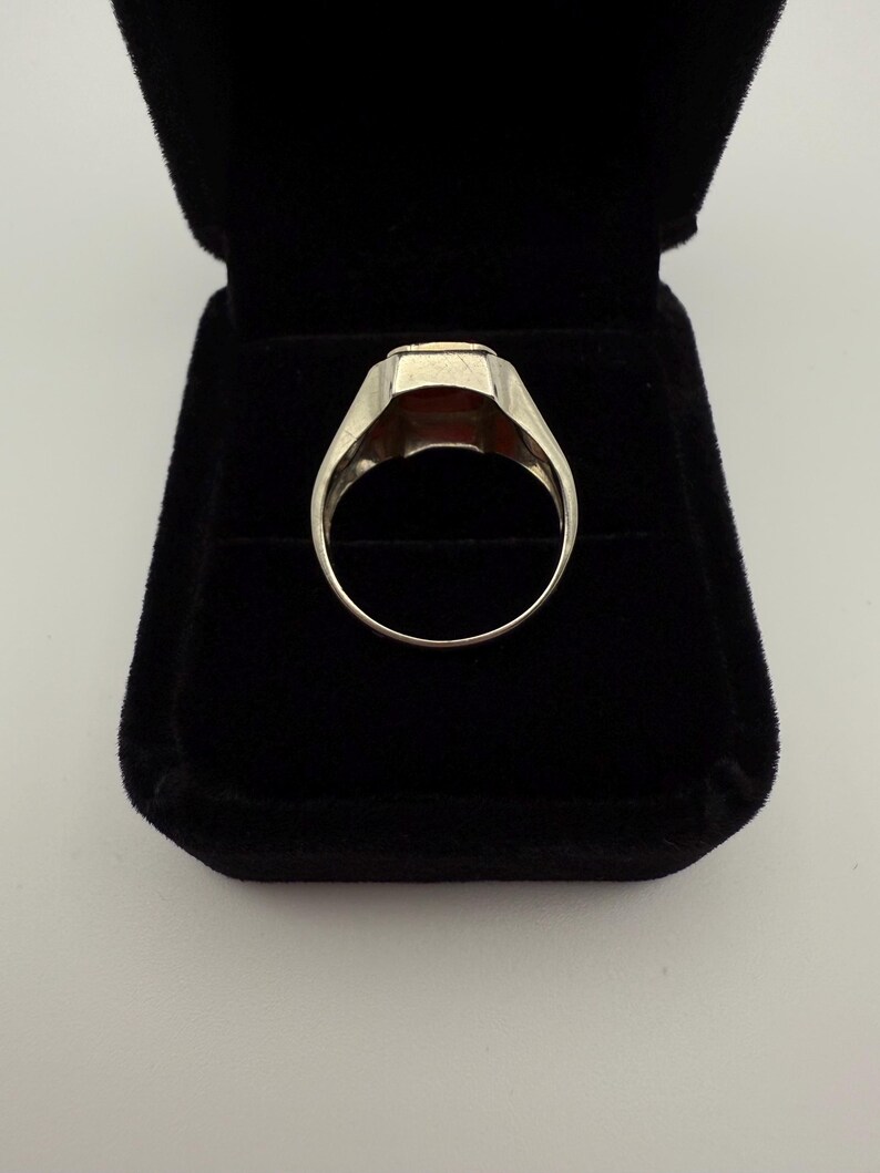May include: A silver ring with a rectangular, reddish-brown stone set in a classic design. The ring is displayed in a black velvet ring box, showcasing its polished metal and gemstone.