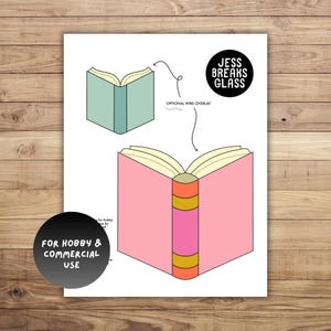 May include: A print featuring two open book illustrations. One book is light green, the other is pink with a pink and gold spine. The text "JESS BREAKS GLASS" is in a black circle. The text "FOR HOBBY & COMMERCIAL USE" is in a black circle.