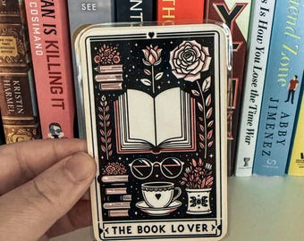 May include: A clear phone case with a black and white illustration of a book, glasses, a cup of tea, and flowers. The text "The Book Lover" is printed on the bottom of the case.
