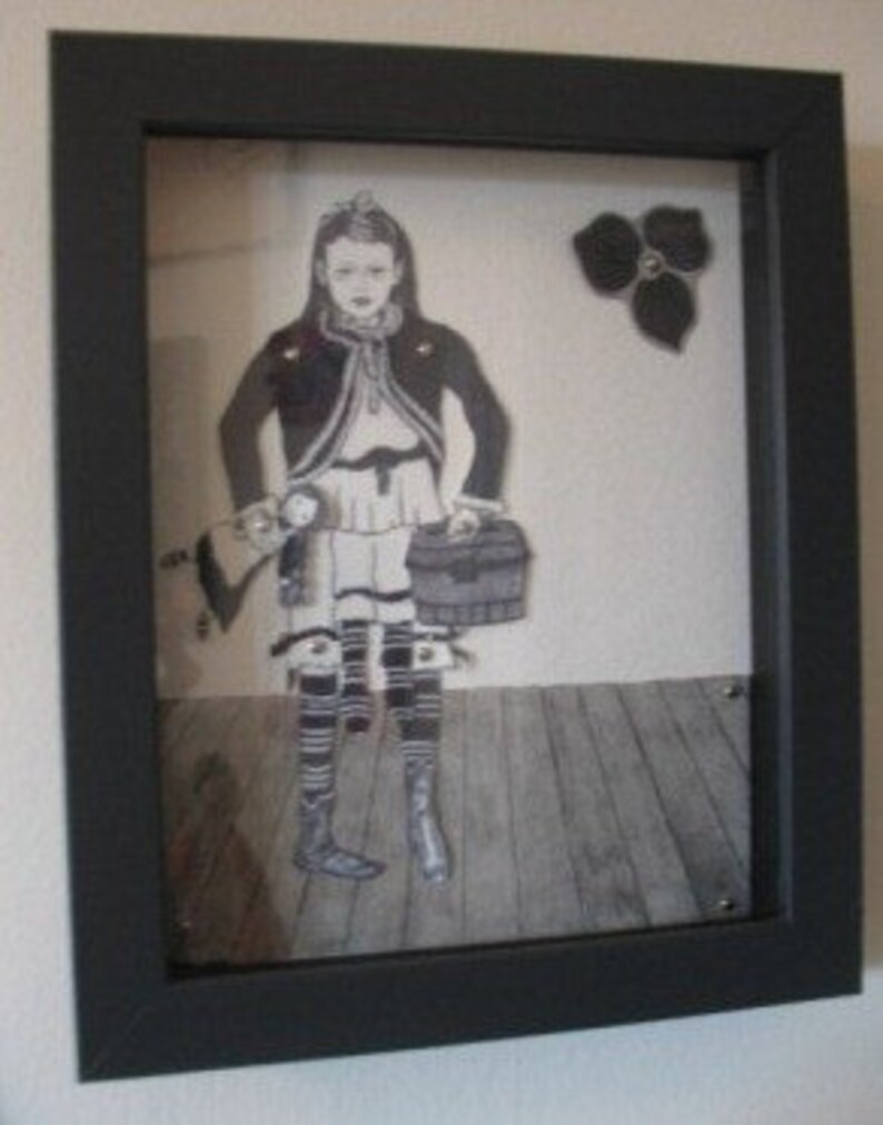 May include: A framed black and white illustration of a girl holding a suitcase and a doll. The girl is wearing a dress, a jacket, and boots. The background is a wooden floor with a black flower in the upper right corner.