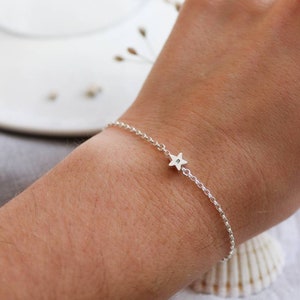 A dainty silver star bracelet shown on a wrist. The silver star has a letter in the centre of it which is personalisable. The star sits in the middle of the wrist on a fine belcher chain.