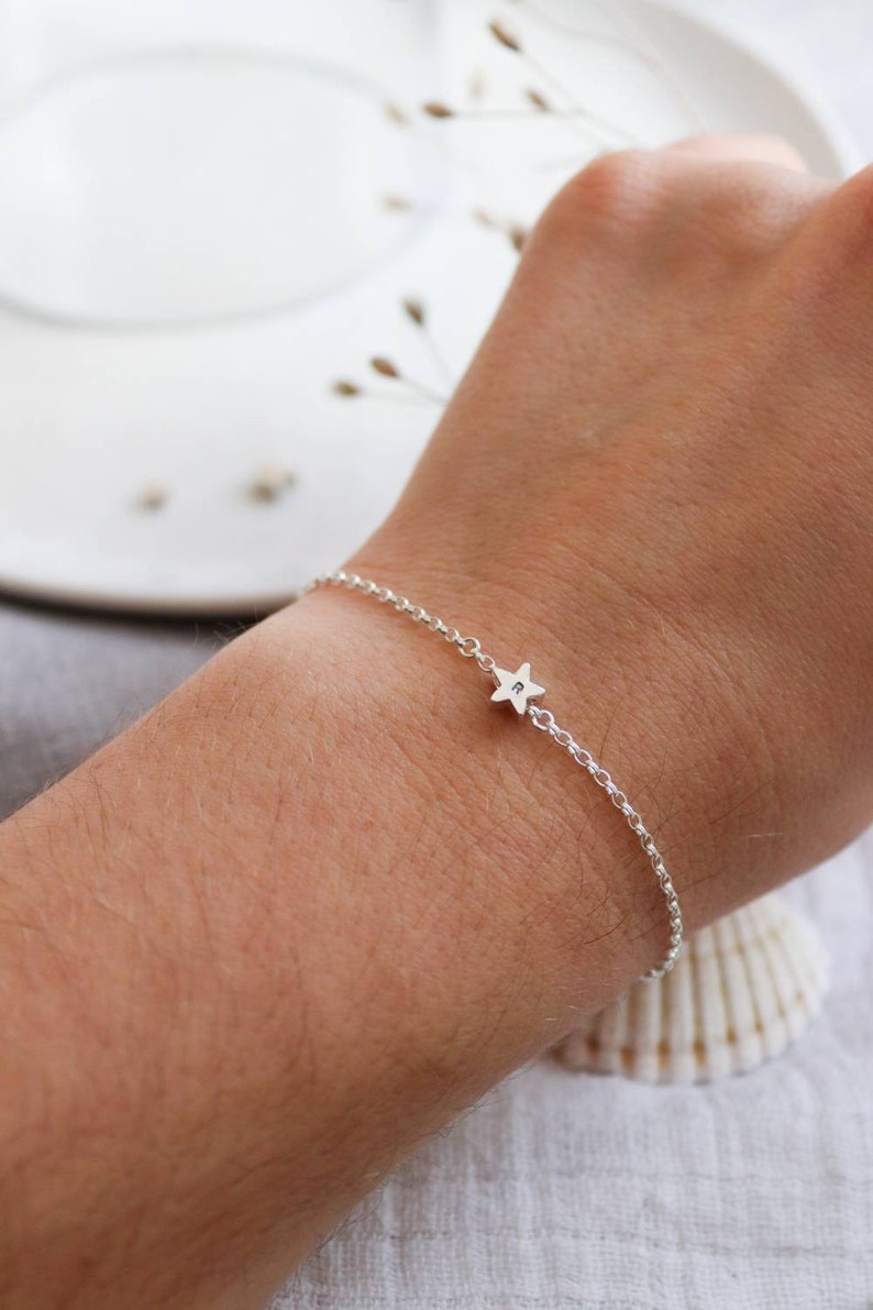 A dainty silver star bracelet shown on a wrist. The silver star has a letter in the centre of it which is personalisable. The star sits in the middle of the wrist on a fine belcher chain.