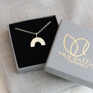 The silver rainbow charm is on a fine chain displayed inside a branded grey jewellery box.