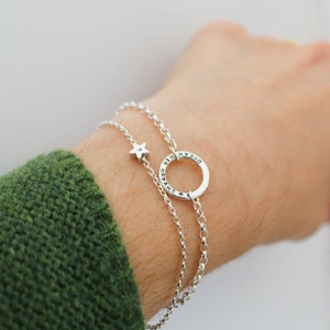 A dainty star bracelet it show on a wrist alongside one of the circle bracelets with message engraved around it. This combination looks lovely together.