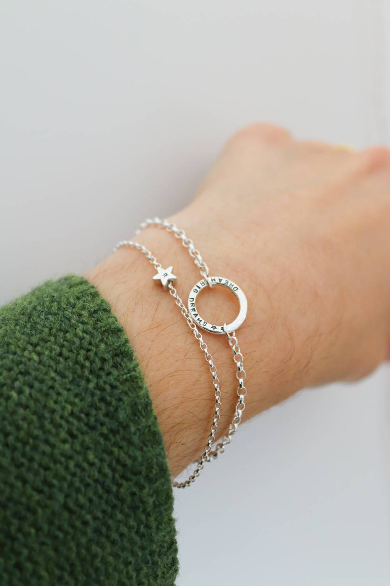 A dainty star bracelet it show on a wrist alongside one of the circle bracelets with message engraved around it. This combination looks lovely together.