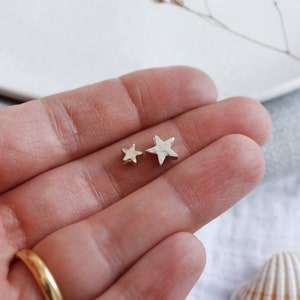 A hand holds to silver stars with a hammered texture. This is the largest and the smallest star, there are three sizes to choose from.