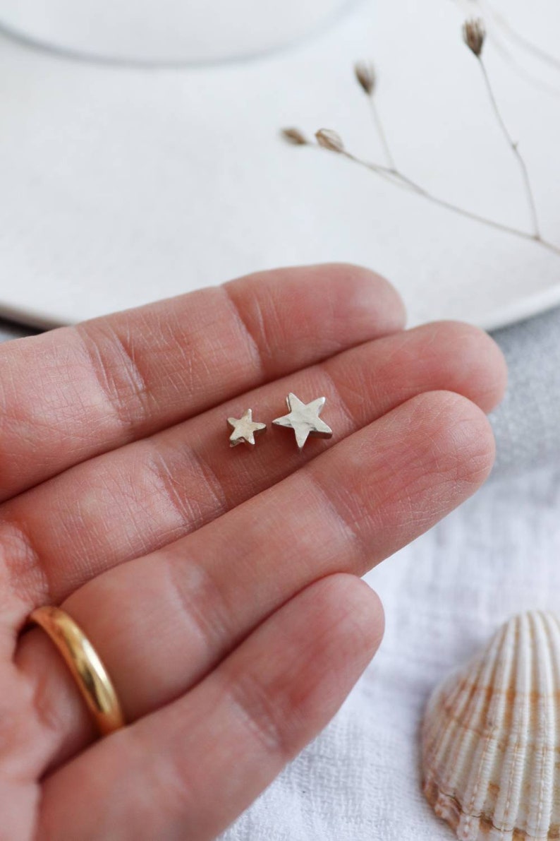 A hand holds to silver stars with a hammered texture. This is the largest and the smallest star, there are three sizes to choose from.