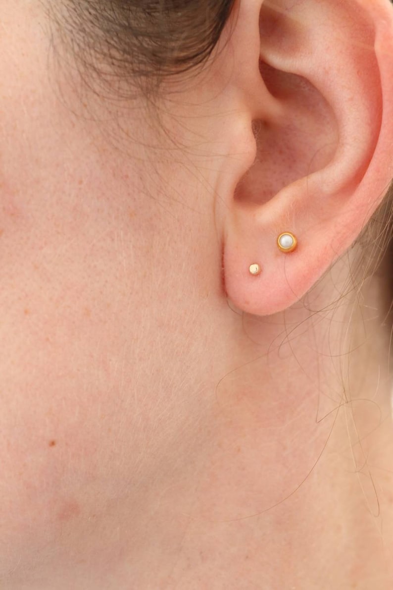 The smaller 2.5mm tiny gold dot stud shown in the main lobe piercing with another larger stud in the second lobe piercing to show scale.