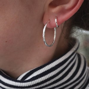 May include: A pair of silver hoop earrings, one larger than the other, worn in a person's earlobe.