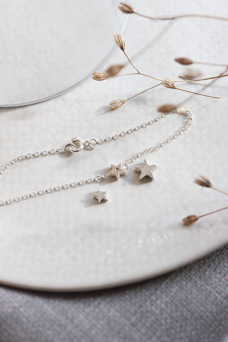 A dainty silver bracelet has the middle sized star at the centre of it with an initial engraved. Next to this is the small and large star to show the gradual increase in size.