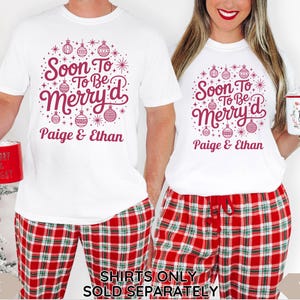 May include: White t-shirts with a festive design that reads "Soon To Be Merry'd" in burgundy, paired with red plaid pajama pants. The design includes ornaments and the names "Paige & Ethan". A red mug is held in each hand.