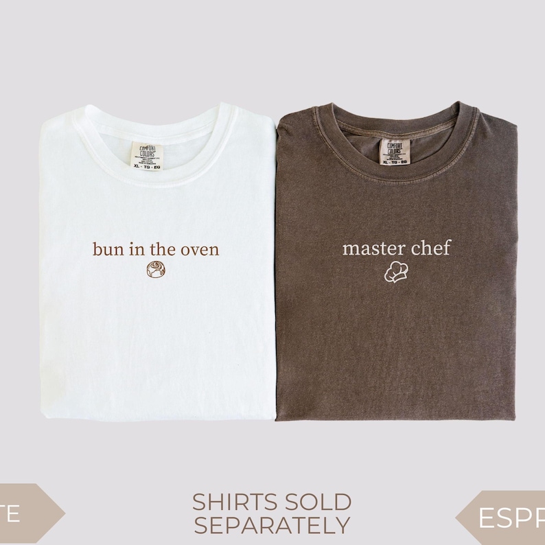 Two folded Comfort Colors t-shirts shown side by side on a light background. The white shirt reads “bun in the oven” in brown text with a small cinnamon roll graphic underneath. The espresso brown shirt reads “master chef” in white text with a small chef hat illustration. Matching pregnancy announcement shirts designed for couples to use for a baby reveal.