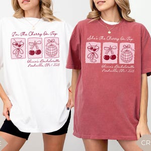 May include: White and crimson t-shirts with a graphic design featuring cocktail glasses, cherries, and a disco ball. The text "I'm The Cherry On Top" and "She's The Cherry On Top" is displayed above the graphics, with "Olivia's Bachelorette Nashville, TN 2026" below.