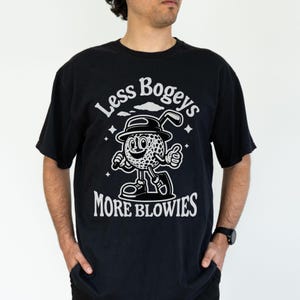 man standing wearing black comfort colors shirt that says less bogeys more blowies with a graphic of a golf ball cartoon holding a club wearing a hat