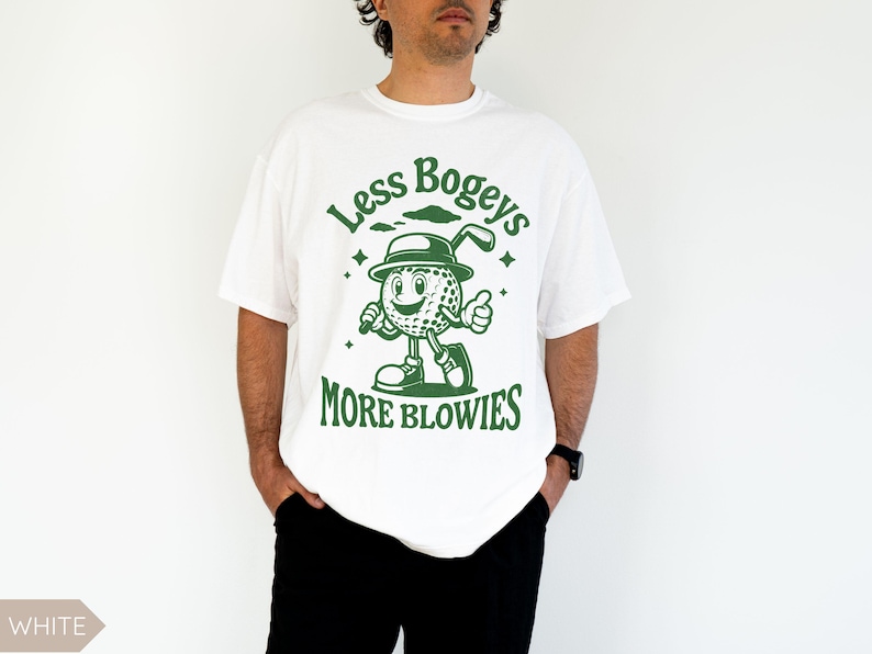 May include: White t-shirt with a green graphic of a cartoon golf ball wearing a hat and holding a golf club. The text "Less Bogeys More Blowies" is printed on the shirt.