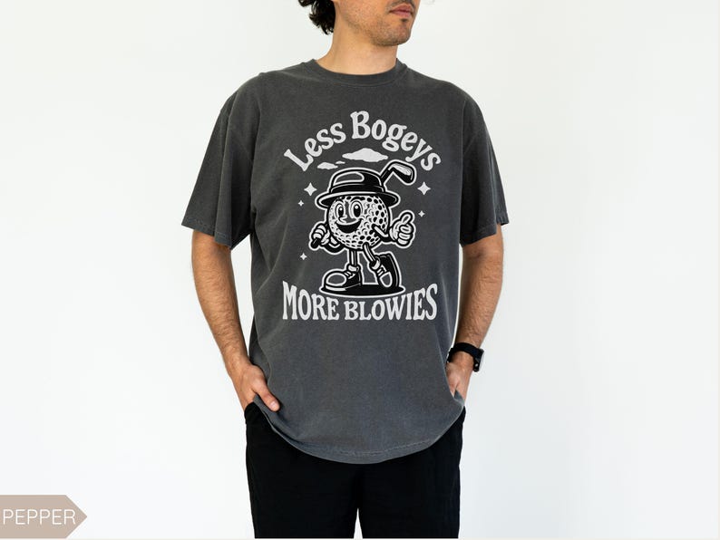 May include: A dark gray t-shirt with a white graphic of a cartoon golf ball character holding a golf club. The text "Less Bogeys More Blowies" is printed on the shirt.