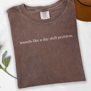 May include: A brown t-shirt with the text "sounds like a day shift problem." printed in white.