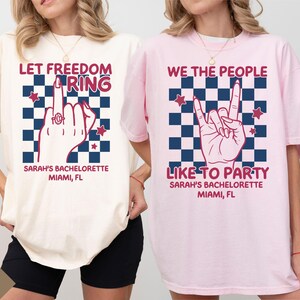 May include: Ivory and pink t-shirts with graphic designs. One shirt says "Let Freedom Ring" with a hand gesture and text "Sarah's Bachelorette Miami, FL." The other says "We The People Like To Party" with a hand gesture and text "Sarah's Bachelorette Miami, FL."
