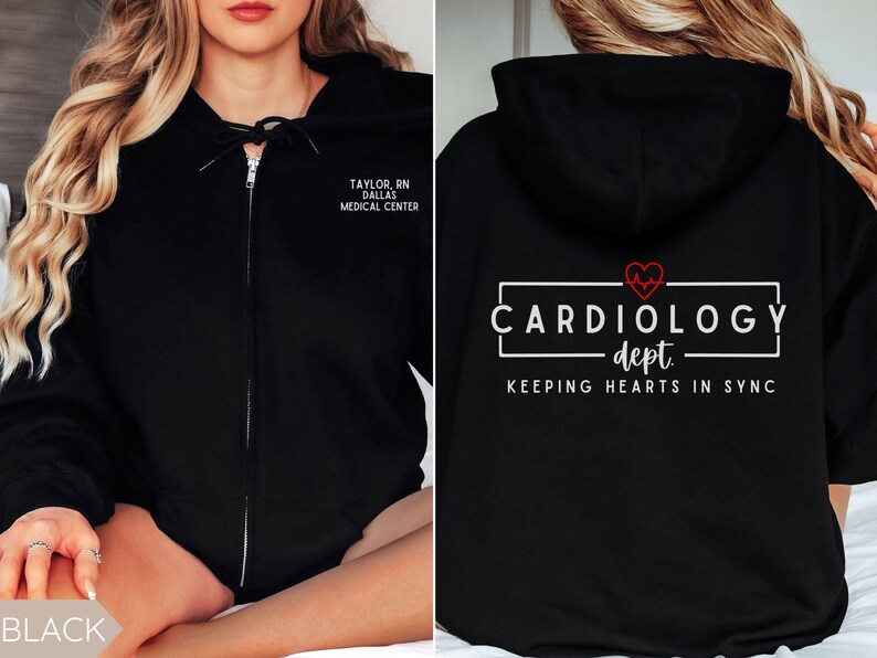 May include: Black zip-up hoodie with a white graphic that says "Cardiology dept. Keeping hearts in sync" with a red heart and EKG line. The hoodie also has white text that says "Taylor, RN Dallas Medical Center".