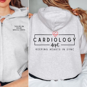 woman sitting wearing an ash zip up hoodie showing front and back. front is personalized name back says cardiology dept keeping hearts in synch