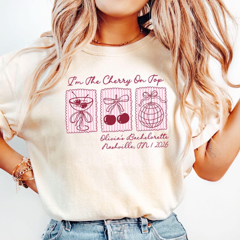 Comfort Colors Ivory bachelorette party t-shirt featuring pink retro stamp-style graphics with cherries, a martini glass, and disco ball illustrations. The text reads “I’m the Cherry On Top” with personalized details including the bride’s name, bachelorette event, Nashville Tennessee location, and year. The shirt is worn casually with rolled sleeves and denim, styled for a Nashville bachelorette weekend.